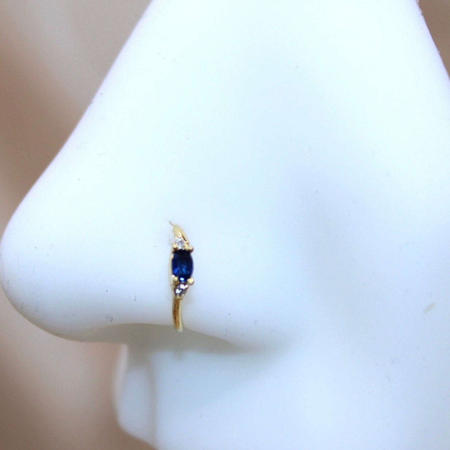 MKBodyJewelry 20g gold nose hoop ring with a central blue marquise gem and two small clear gems.