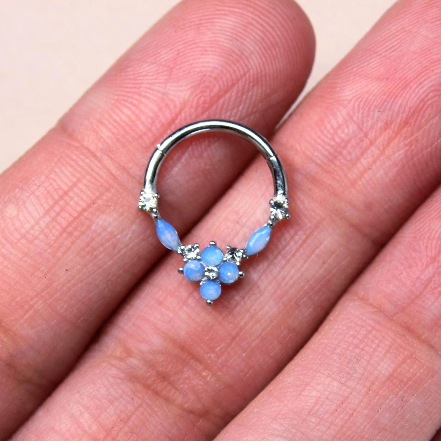 MKBodyJewelry blue opal floral septum clicker ring in surgical steel held between fingers