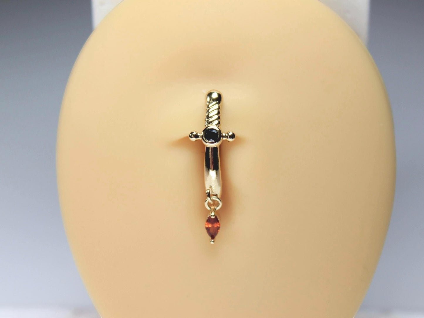 MKBodyJewelry gold-tone stainless steel dagger belly button ring with dangling marquise-cut orange CZ and black gem.