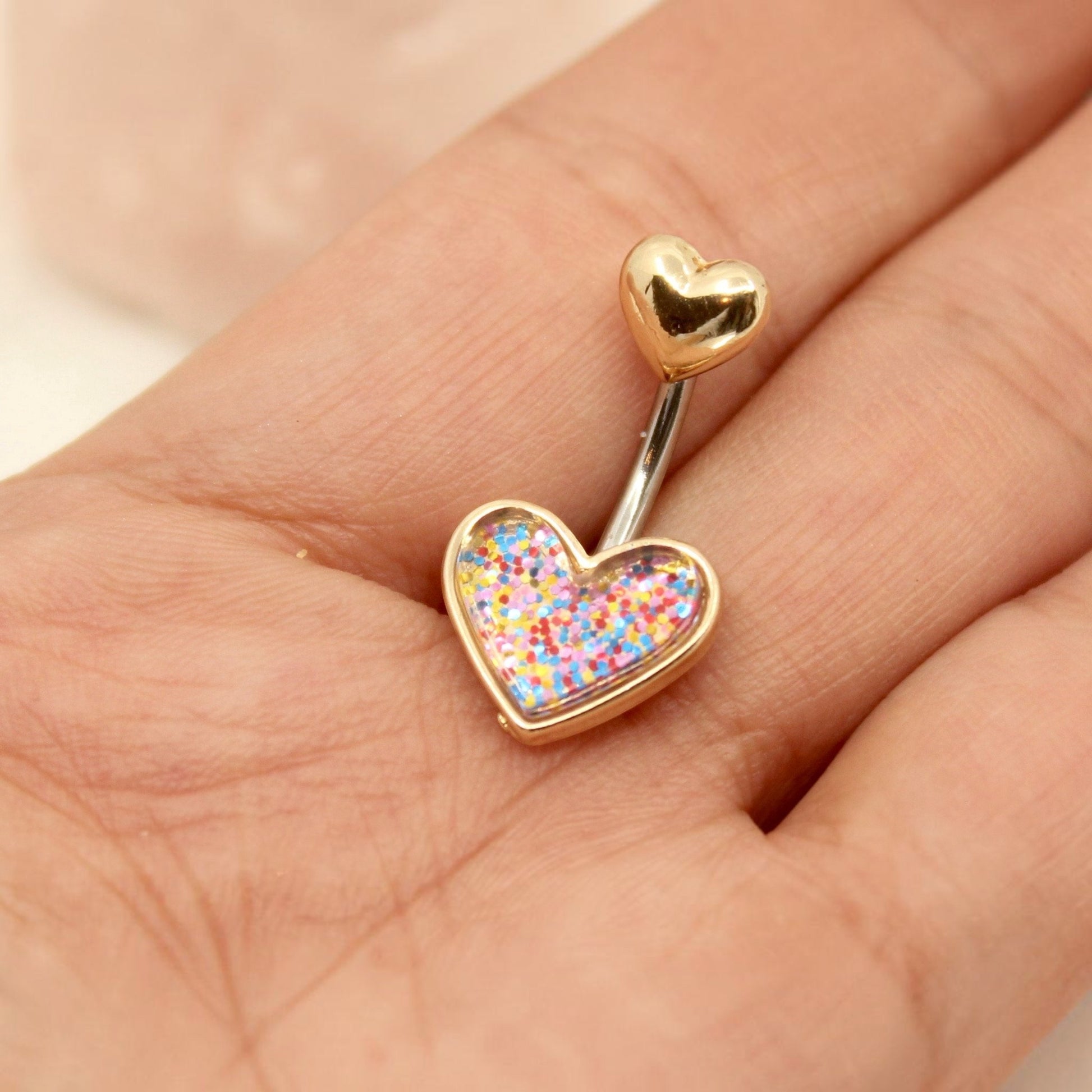 MKBodyJewelry 14G gold surgical steel belly button ring featuring a resin heart charm with colorful glitter.