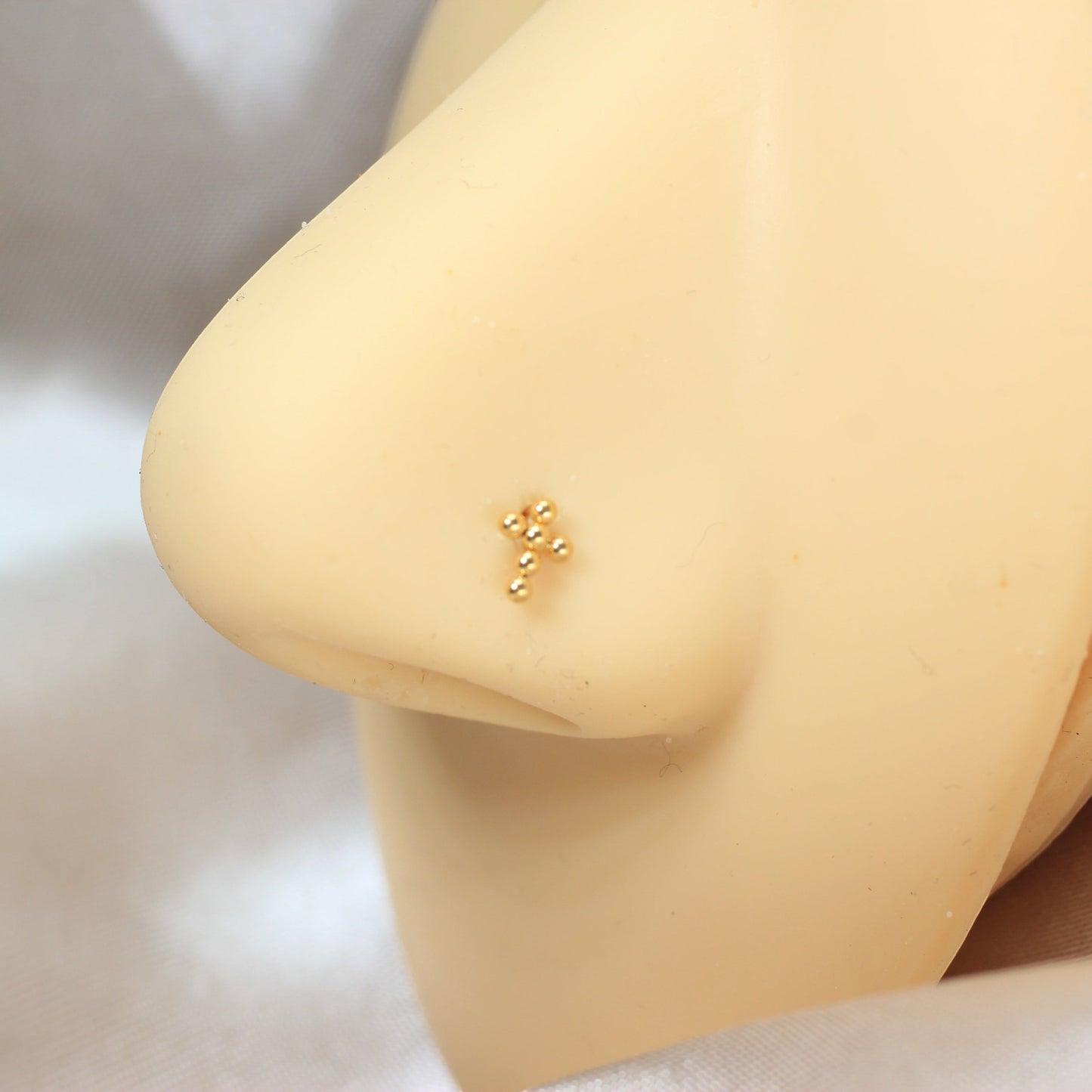 MKBodyJewelry gold beaded cross corkscrew nose stud on a mannequin nose, minimalist titanium body jewelry.