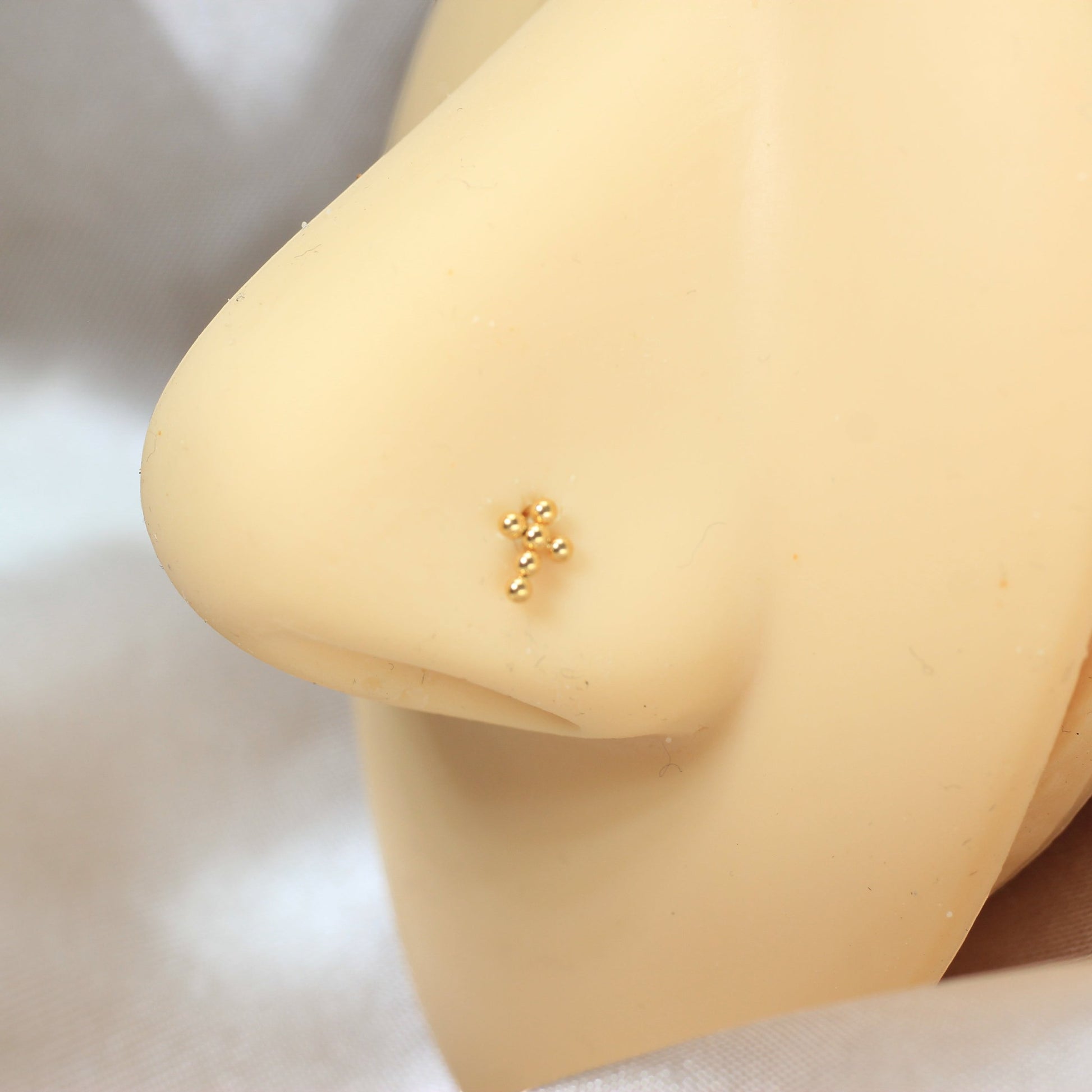 MKBodyJewelry gold beaded cross corkscrew nose stud on a mannequin nose, minimalist titanium body jewelry.