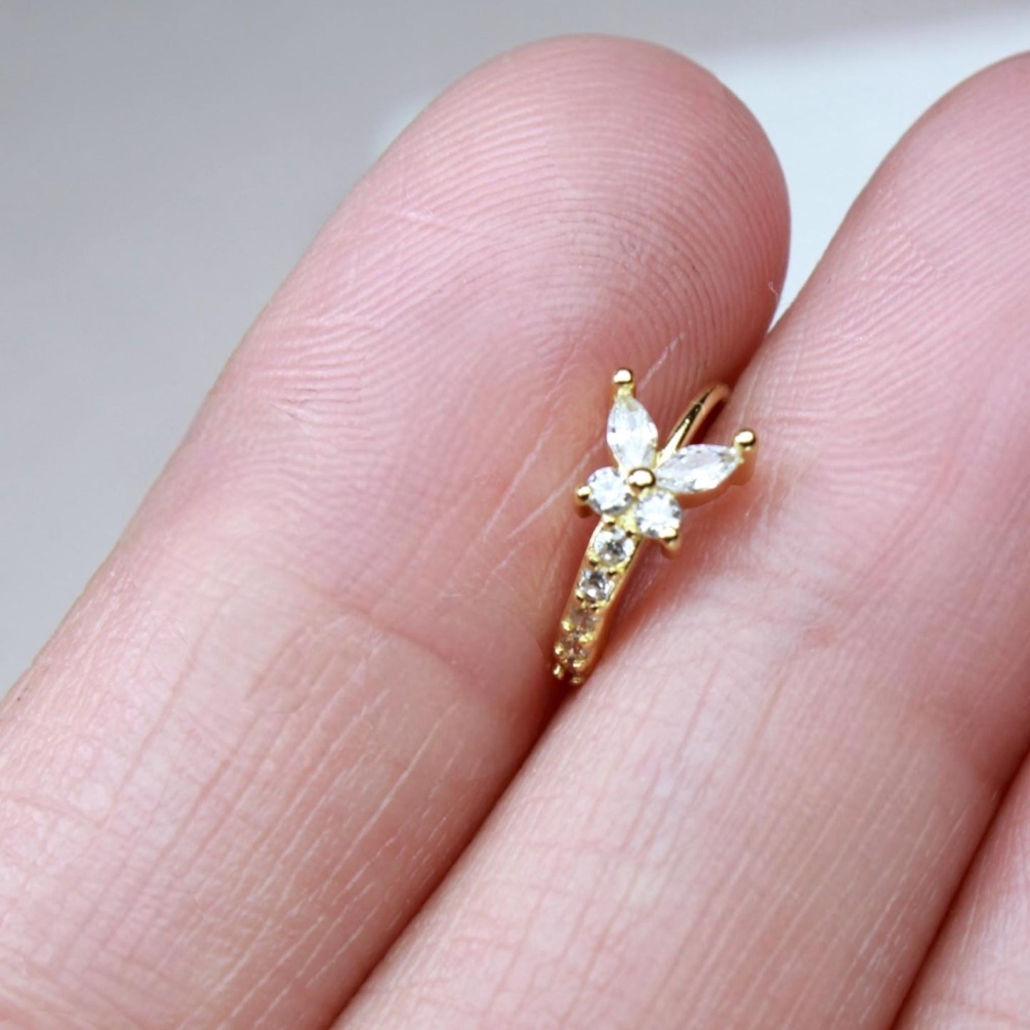 MKBodyJewelry gold butterfly nose hoop ring with sparkling cubic zirconia stones held between fingers