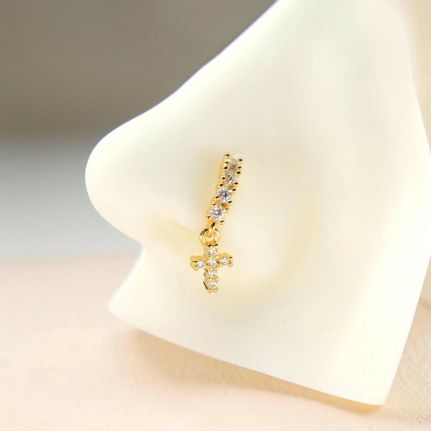 MKBodyJewelry 20g gold surgical steel nose hoop with a dangling CZ cross charm on a white display model