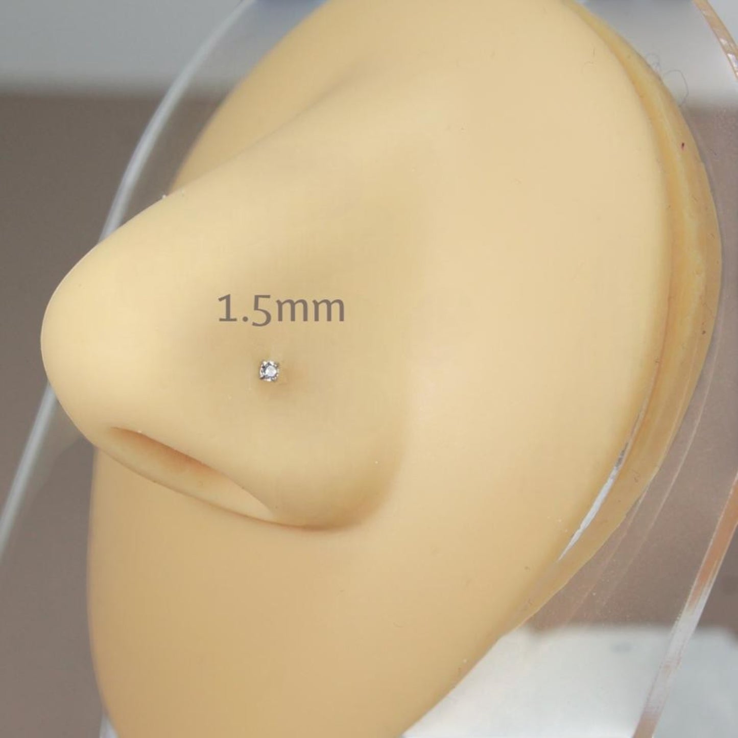 MKBodyJewelry 1.5mm gold-tone nose stud with a round-cut cubic zirconia in a four-prong setting on a mannequin nose.