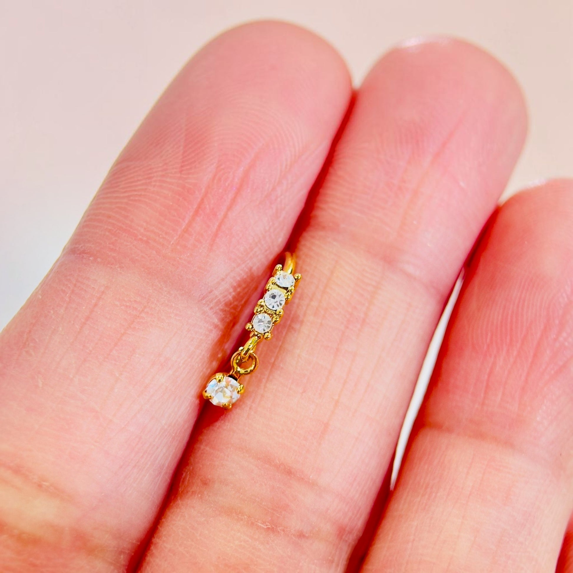 MKBodyJewelry gold surgical steel dangling nose hoop with sparkling CZ gems held between fingers