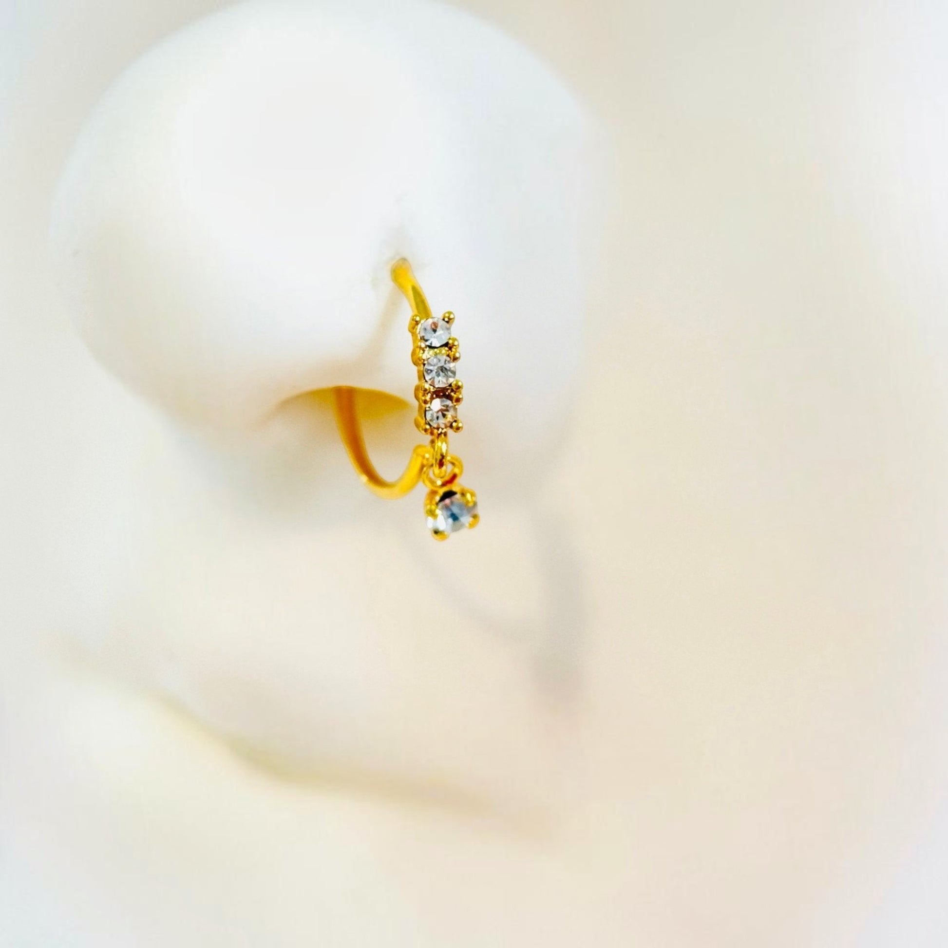 MKBodyJewelry 20g gold surgical steel nose hoop with dangling CZ charm and sparkling crystal accents on a display model