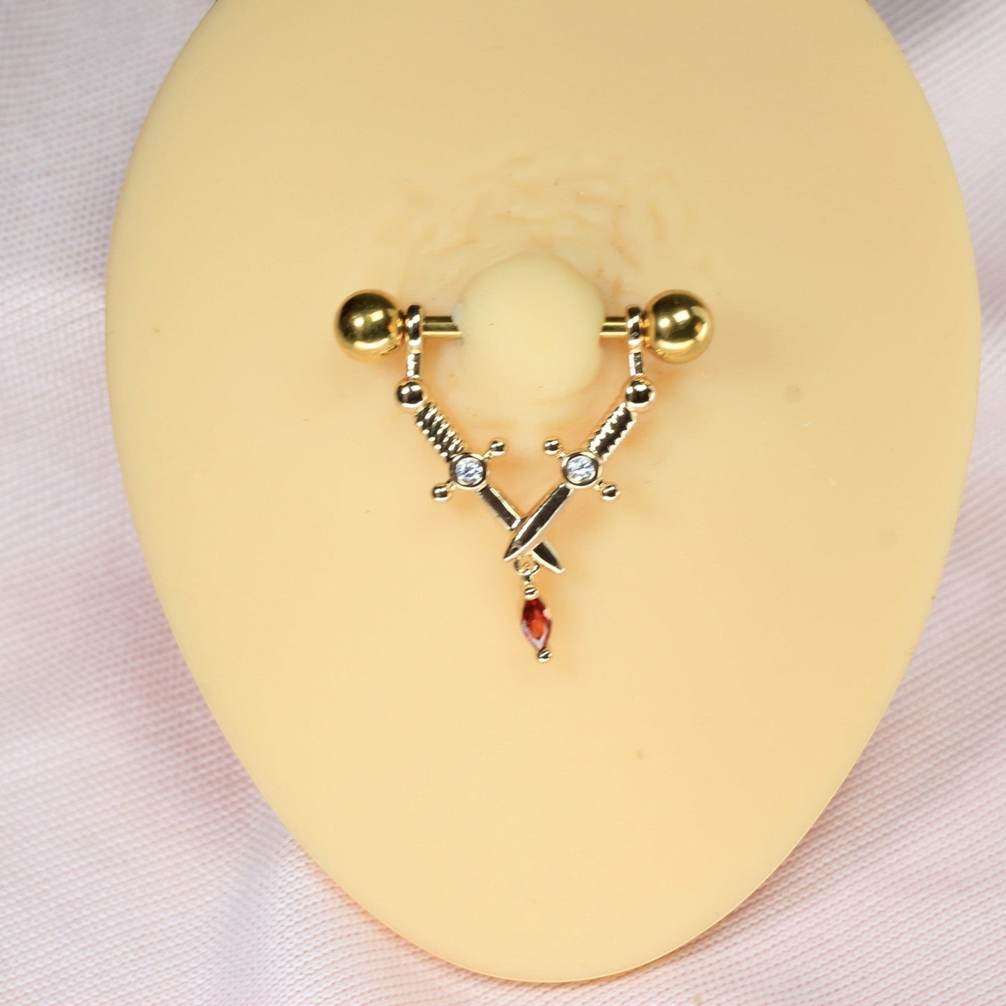 MKBodyJewelry gold dangling dagger nipple barbell pair with surgical steel, sword design, and red crystal accents.