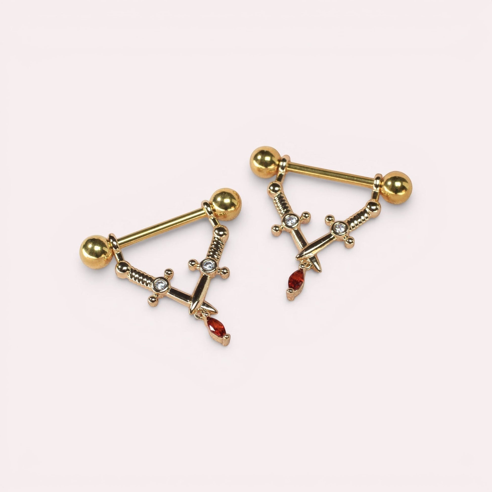 MKBodyJewelry 14g gold surgical steel dangling dagger nipple barbells with clear and red crystal accents.