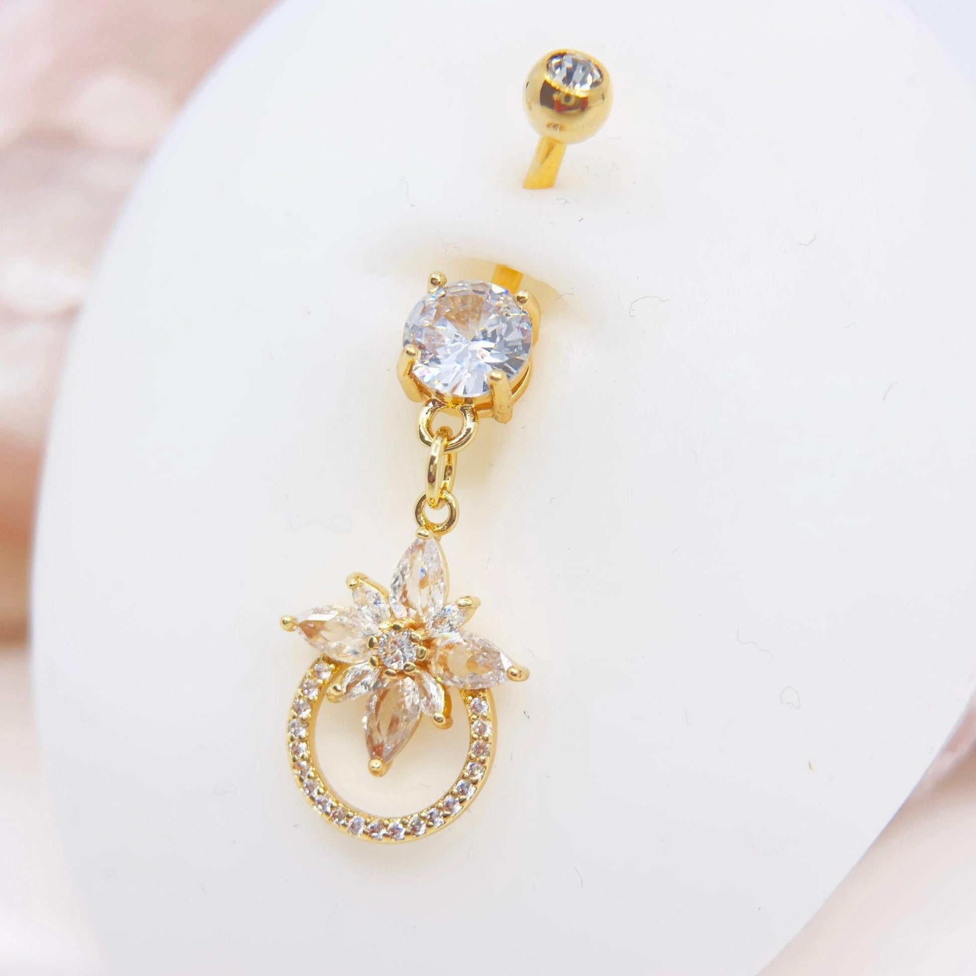 MKBodyJewelry 14g gold surgical steel belly button ring with a dangling floral charm and sparkling CZ stones.