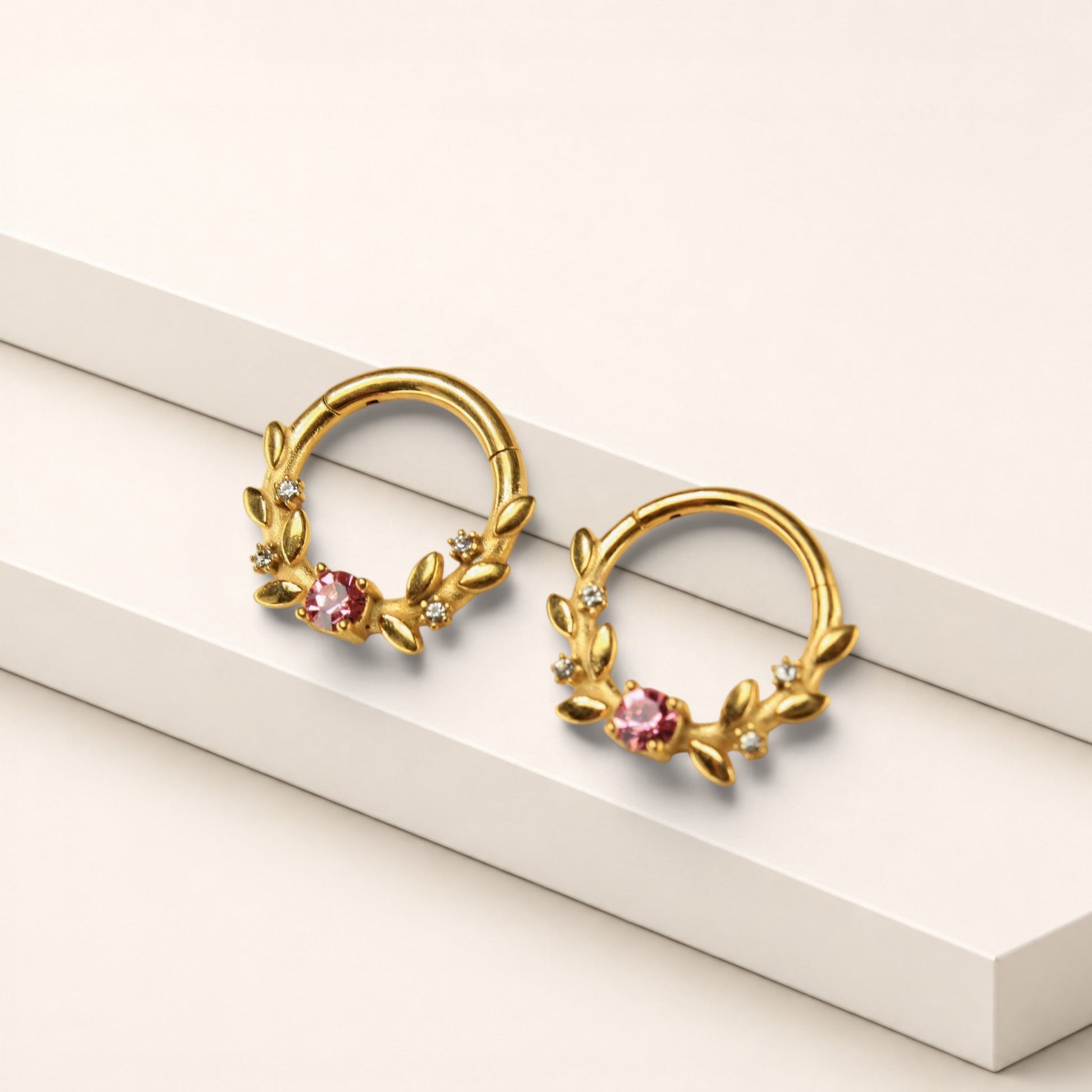 MKBodyJewelry gold surgical steel septum clicker rings with pink floral gem accents on a white display stand.
