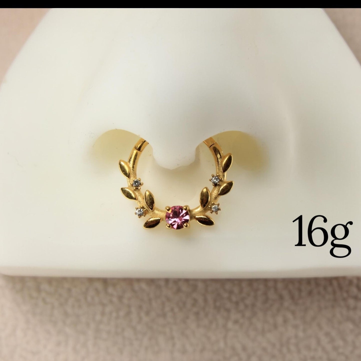 MKBodyJewelry gold floral septum clicker ring with a pink center gem and clear accent stones on a nose display model.