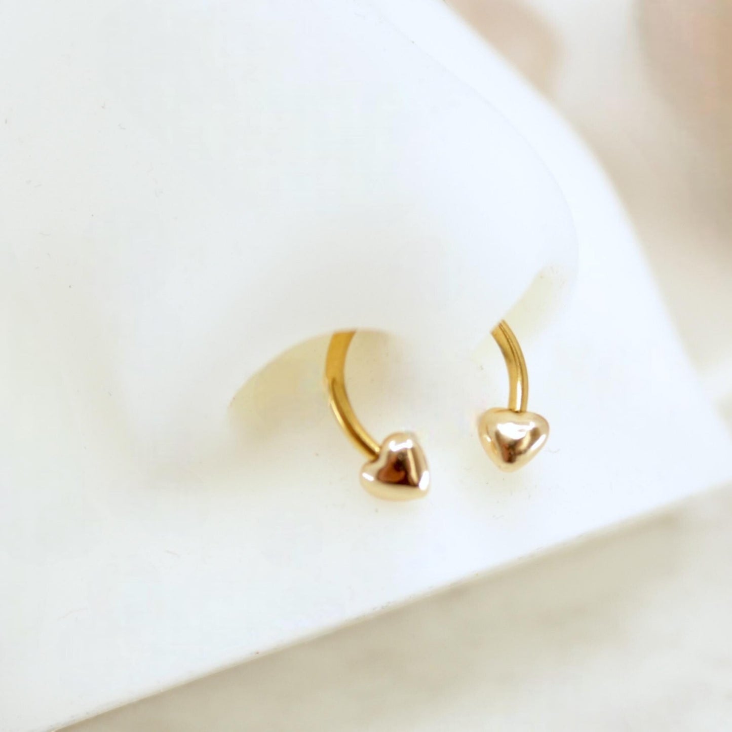 MKBodyJewelry 16G gold surgical steel horseshoe septum ring with heart ends on a white nose display model