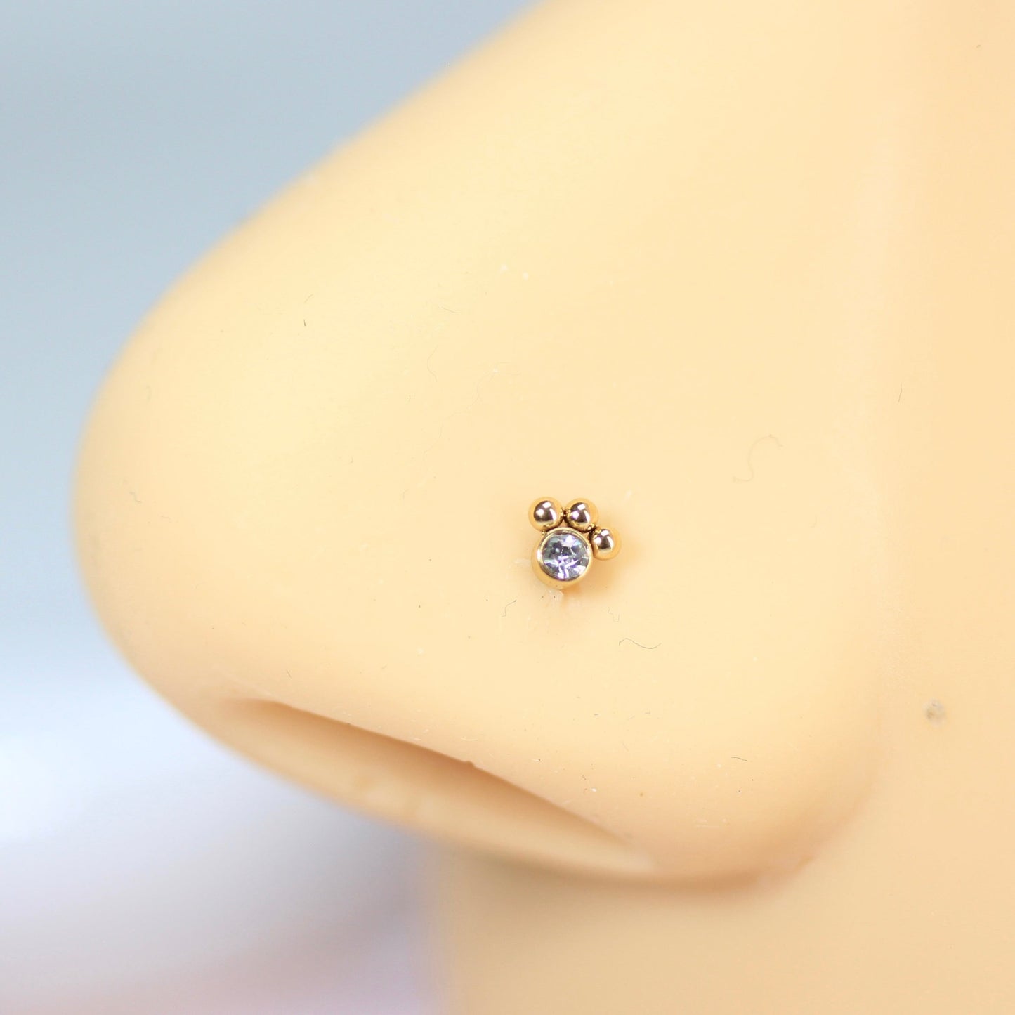 MKBodyJewelry gold paw print nose stud with a clear crystal center on a mannequin nose