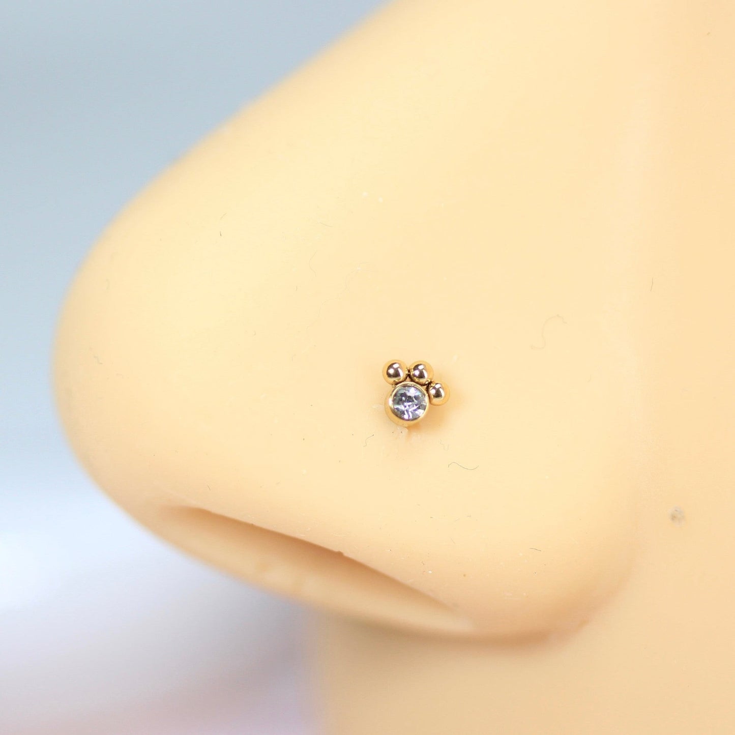 MKBodyJewelry gold paw print nose stud with a clear crystal center on a mannequin nose