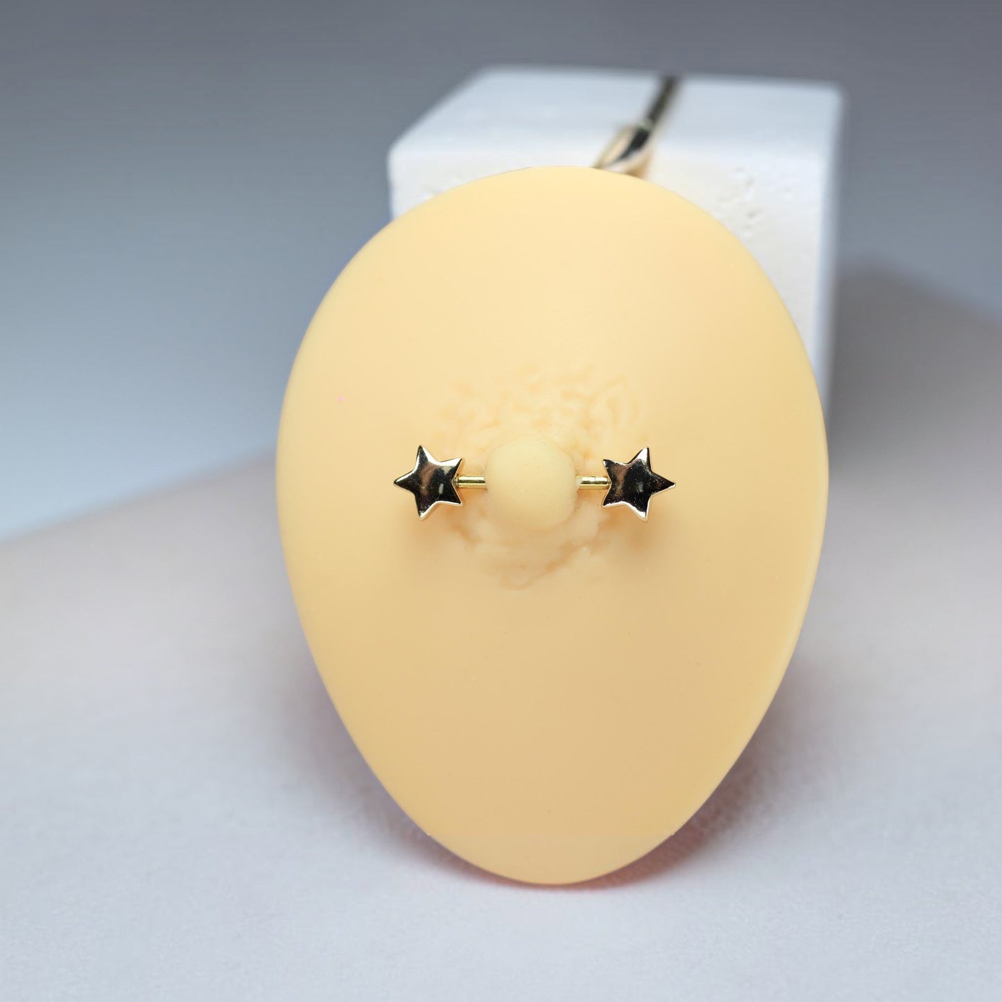 MKBodyJewelry 14G gold star nipple barbell piercing made of hypoallergenic surgical steel on a display model.