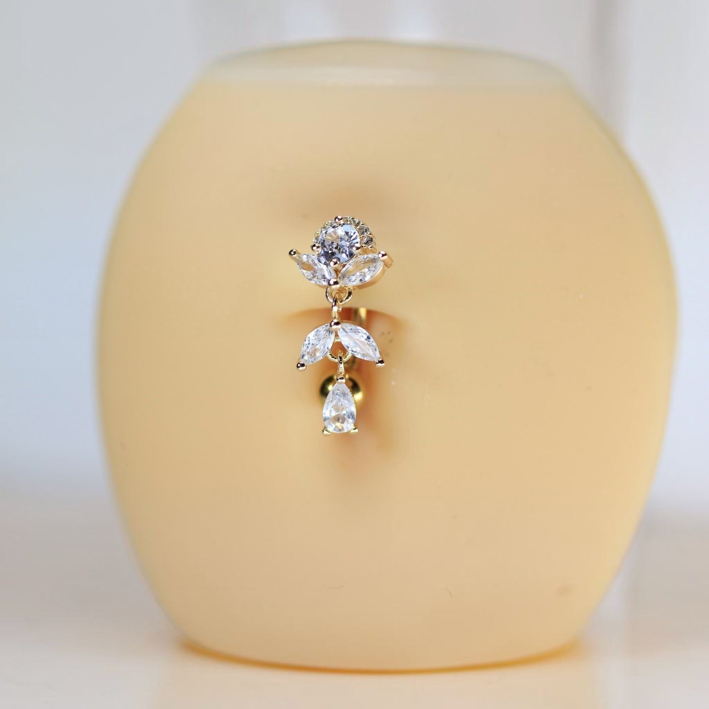MKBodyJewelry gold titanium inverted floral belly button ring with clear CZ stones and a dangling teardrop charm.