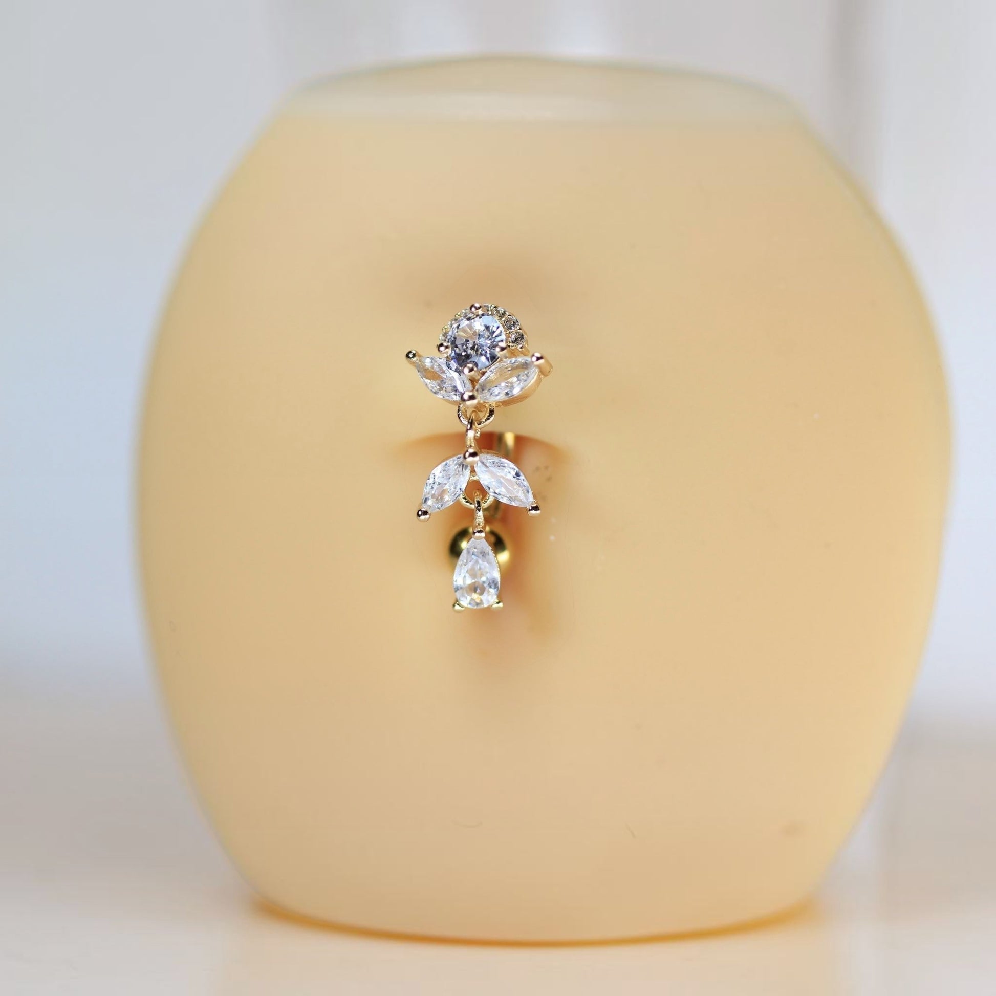 MKBodyJewelry gold titanium inverted floral belly button ring with clear CZ stones and a dangling teardrop charm.