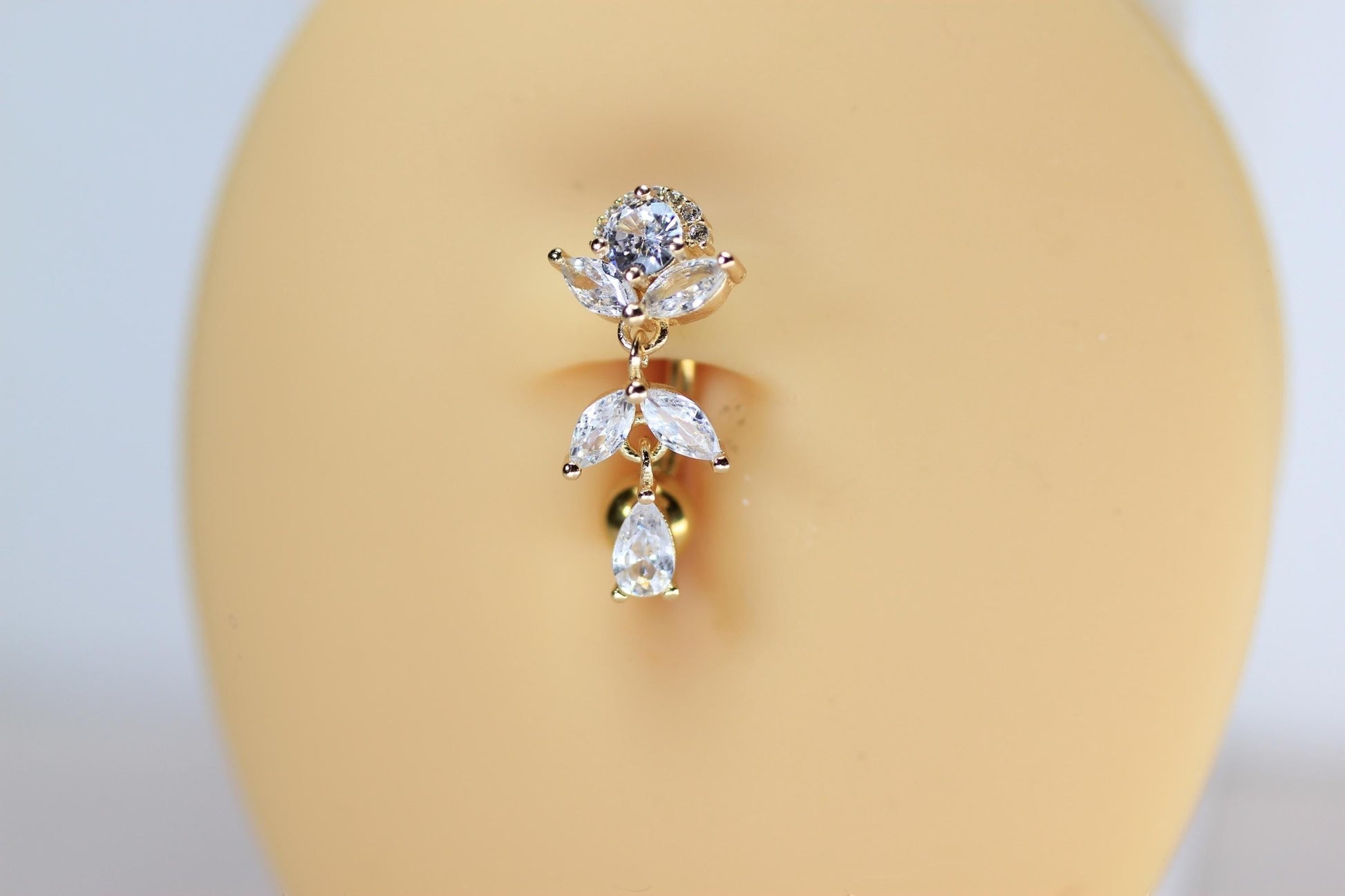 MKBodyJewelry gold titanium inverted floral belly button ring with clear CZ stones and a dangling teardrop charm.