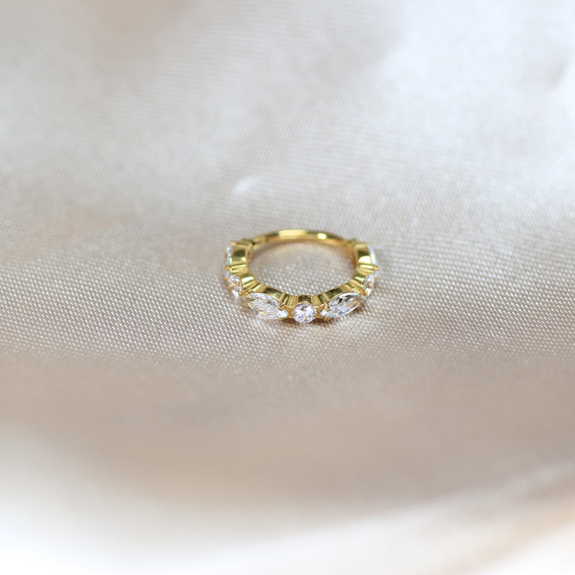 MKBodyJewelry gold titanium hinged nose clicker ring with marquise and round CZ gems on a satin background.