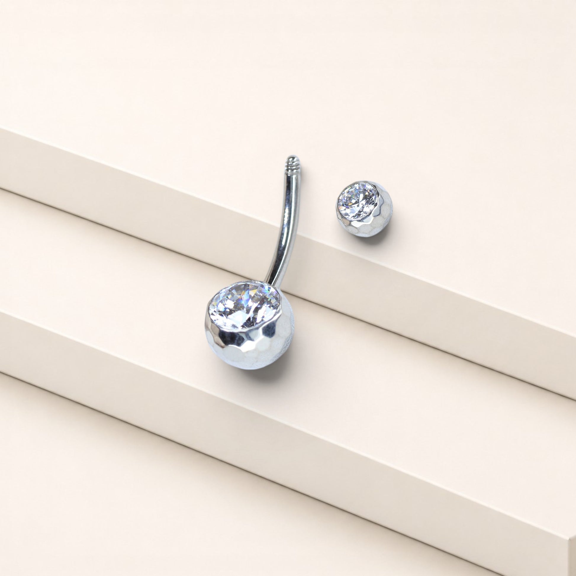 MKBodyJewelry 14g gold titanium belly button ring with a faceted honeycomb CZ setting on a minimalist display