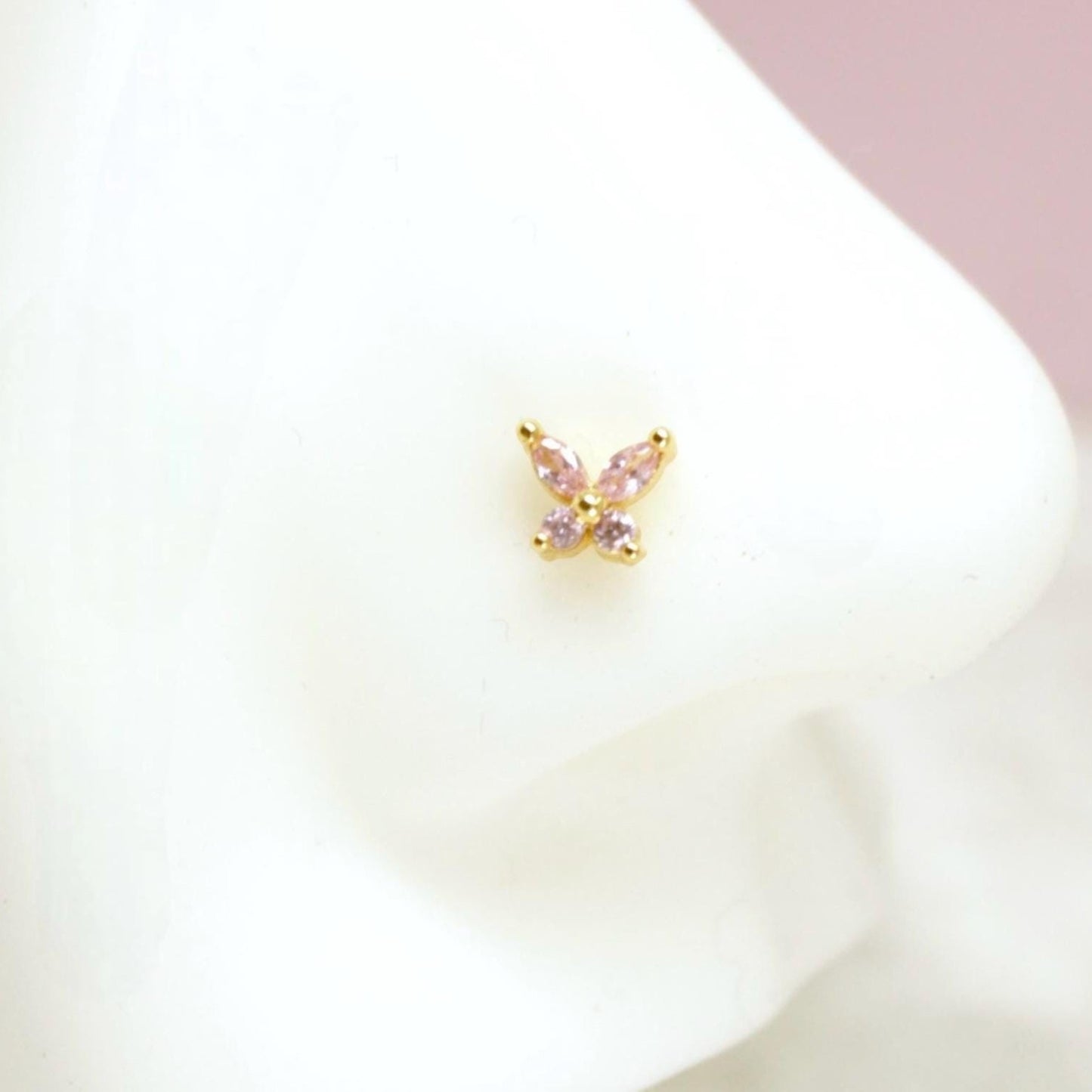 MKBodyJewelry dainty gold nose stud featuring a sparkly pink gemstone butterfly design on a white mannequin nose.