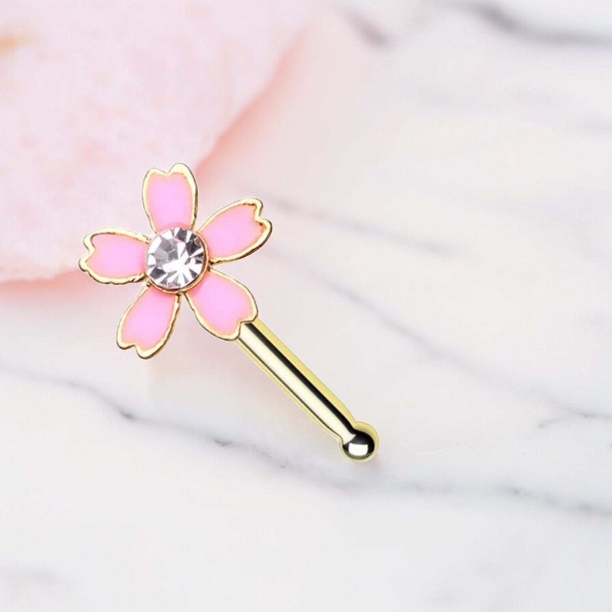 MKBodyJewelry 20G pink flower nose bone stud in surgical steel with a central crystal gem on a marble background