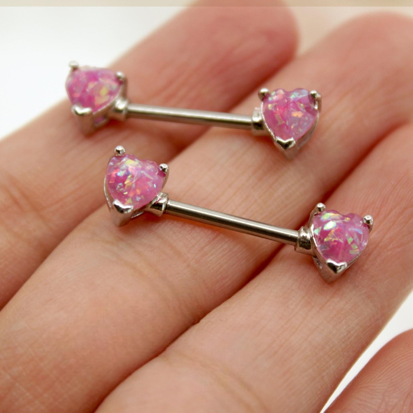MKBodyJewelry 14g surgical steel nipple rings featuring pink opal heart ends held in a hand.