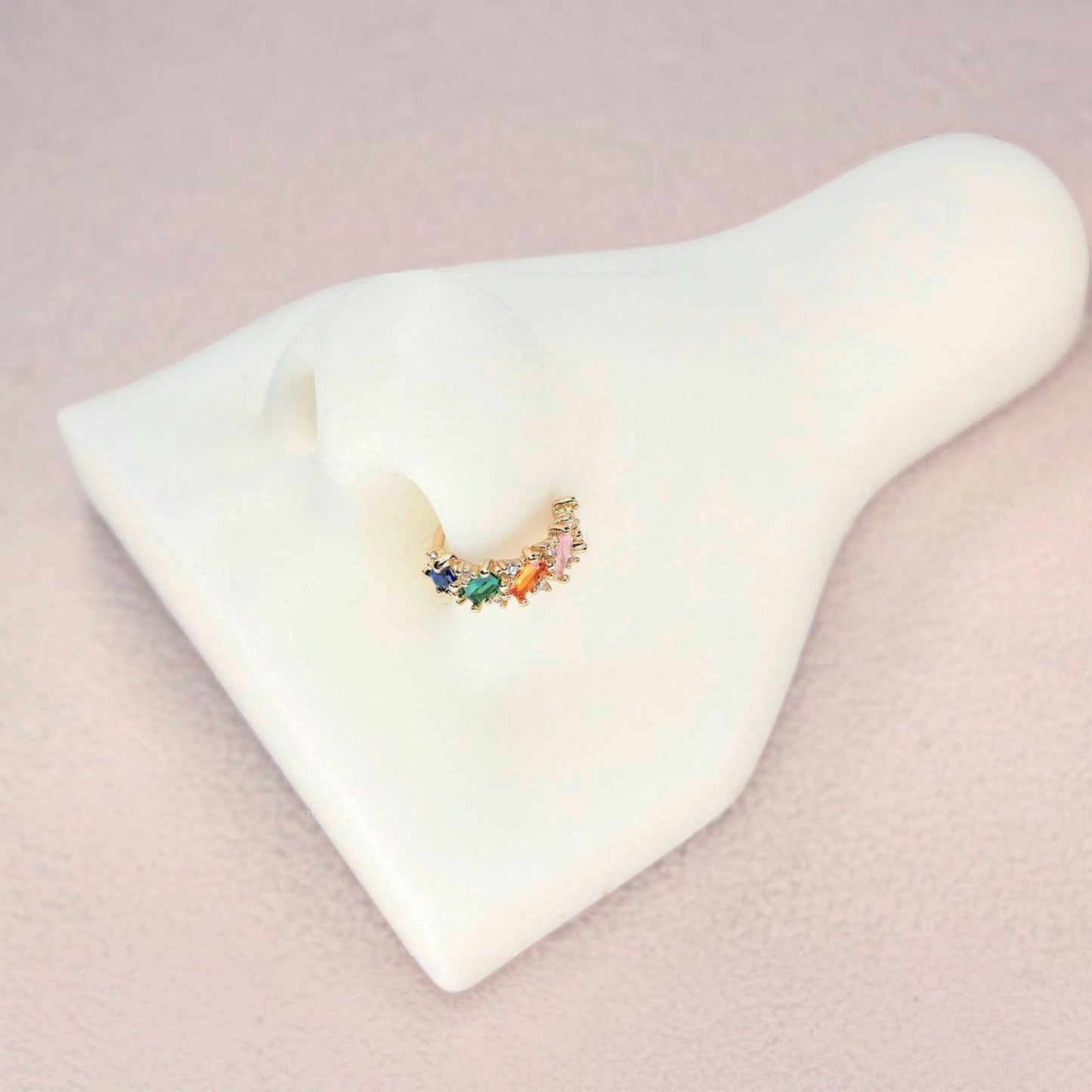 MKBodyJewelry 20g gold nose hoop with rainbow baguette cubic zirconia stones on a white nose display model.