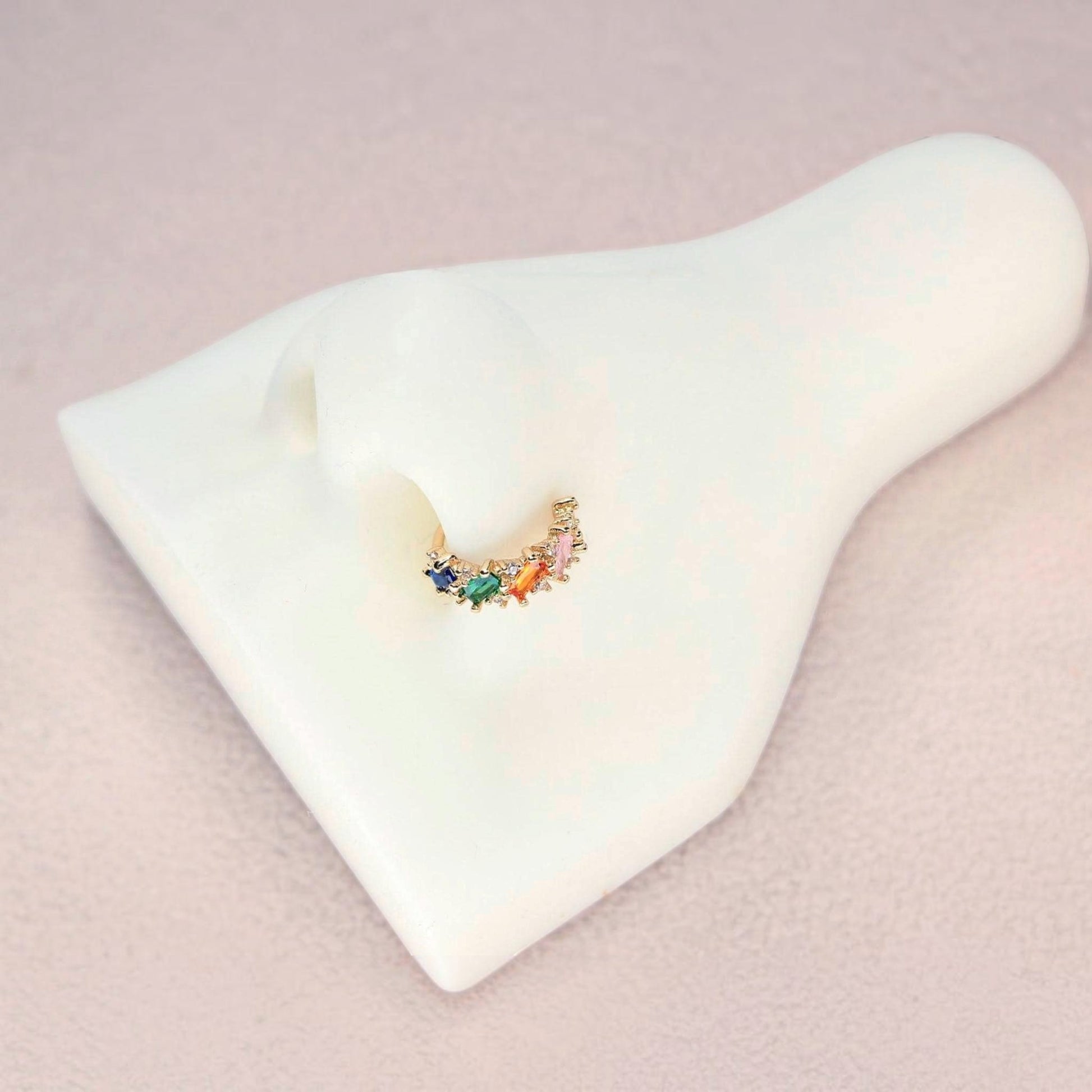 MKBodyJewelry 20g gold nose hoop with rainbow baguette cubic zirconia stones on a white nose display model.