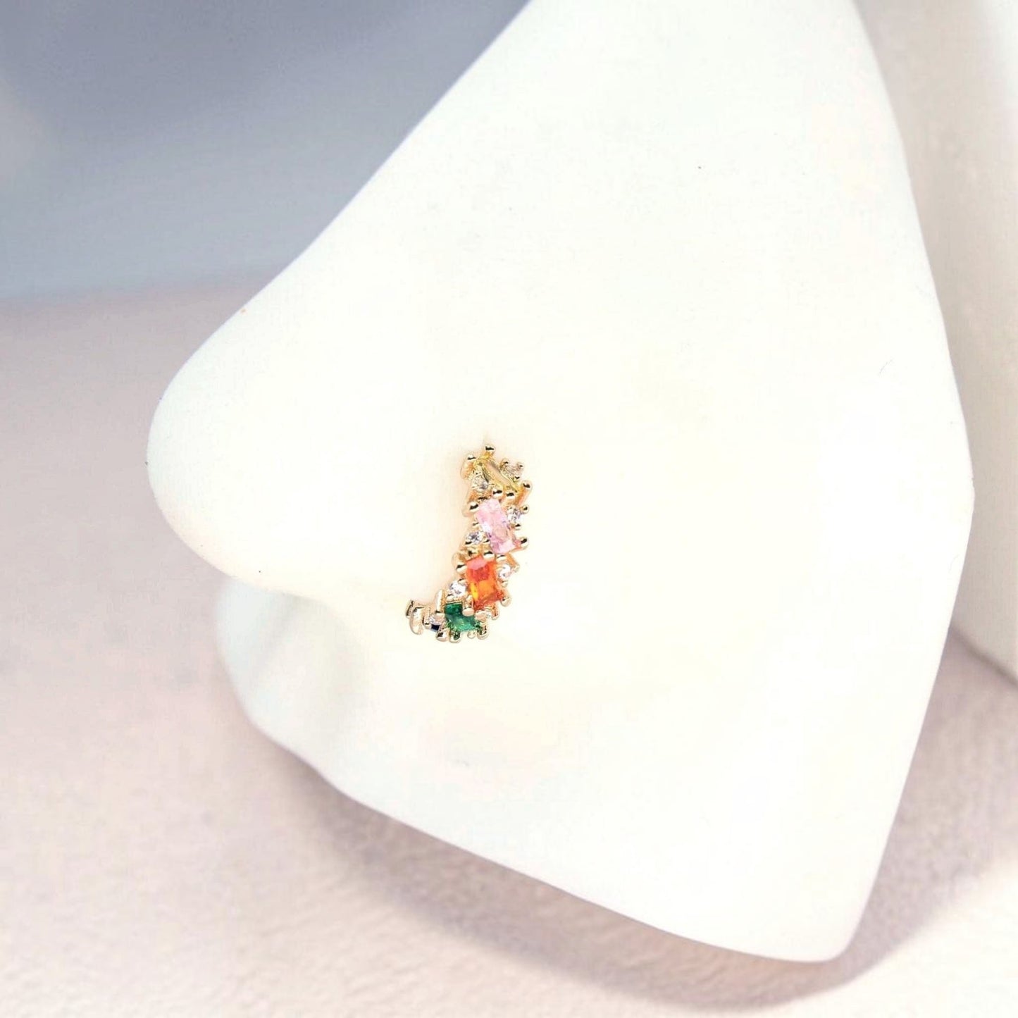 MKBodyJewelry 20g gold nose hoop with rainbow baguette cubic zirconia stones on a white mannequin nose display.