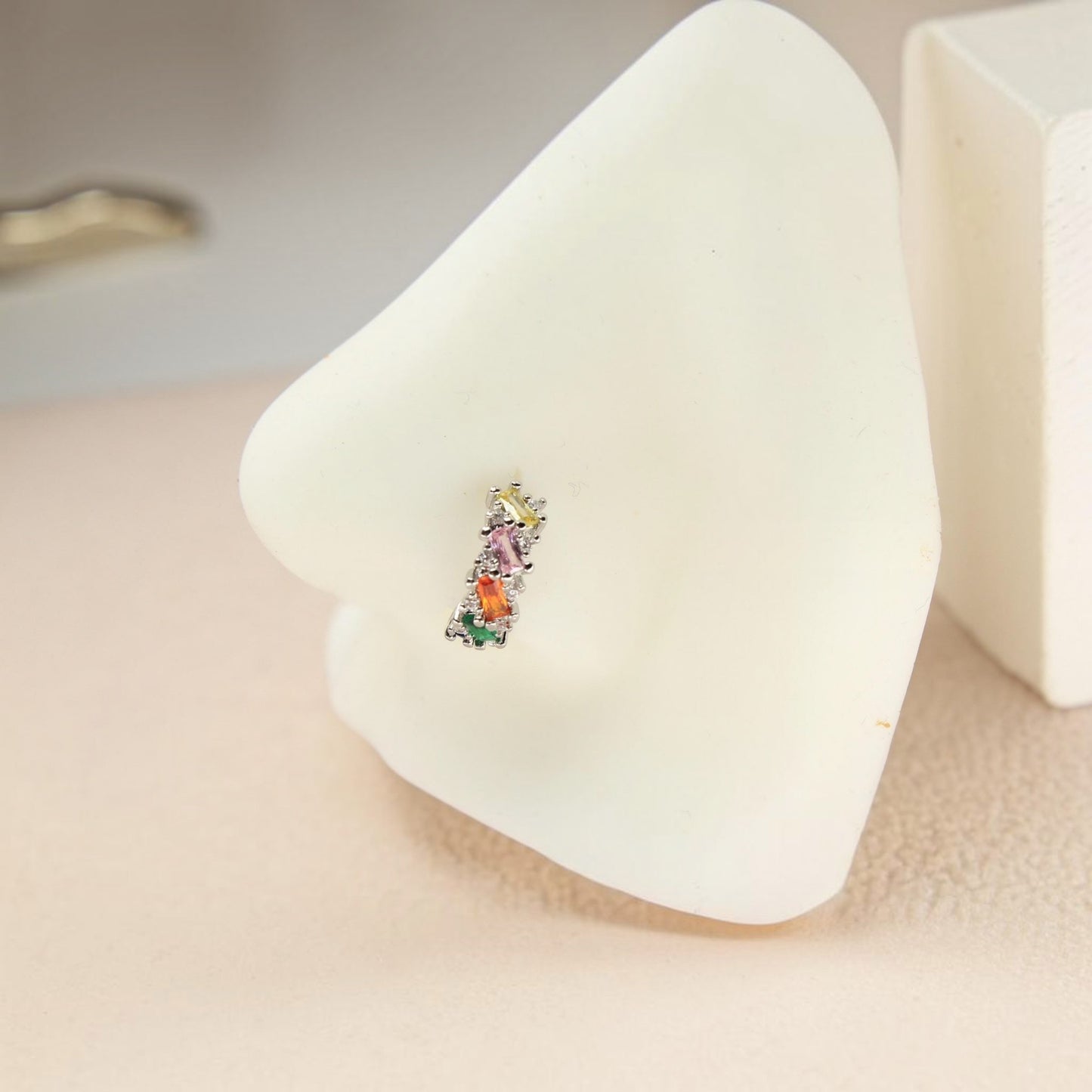 MKBodyJewelry 20g gold nose hoop with rainbow baguette cubic zirconia stones on a white nose display model