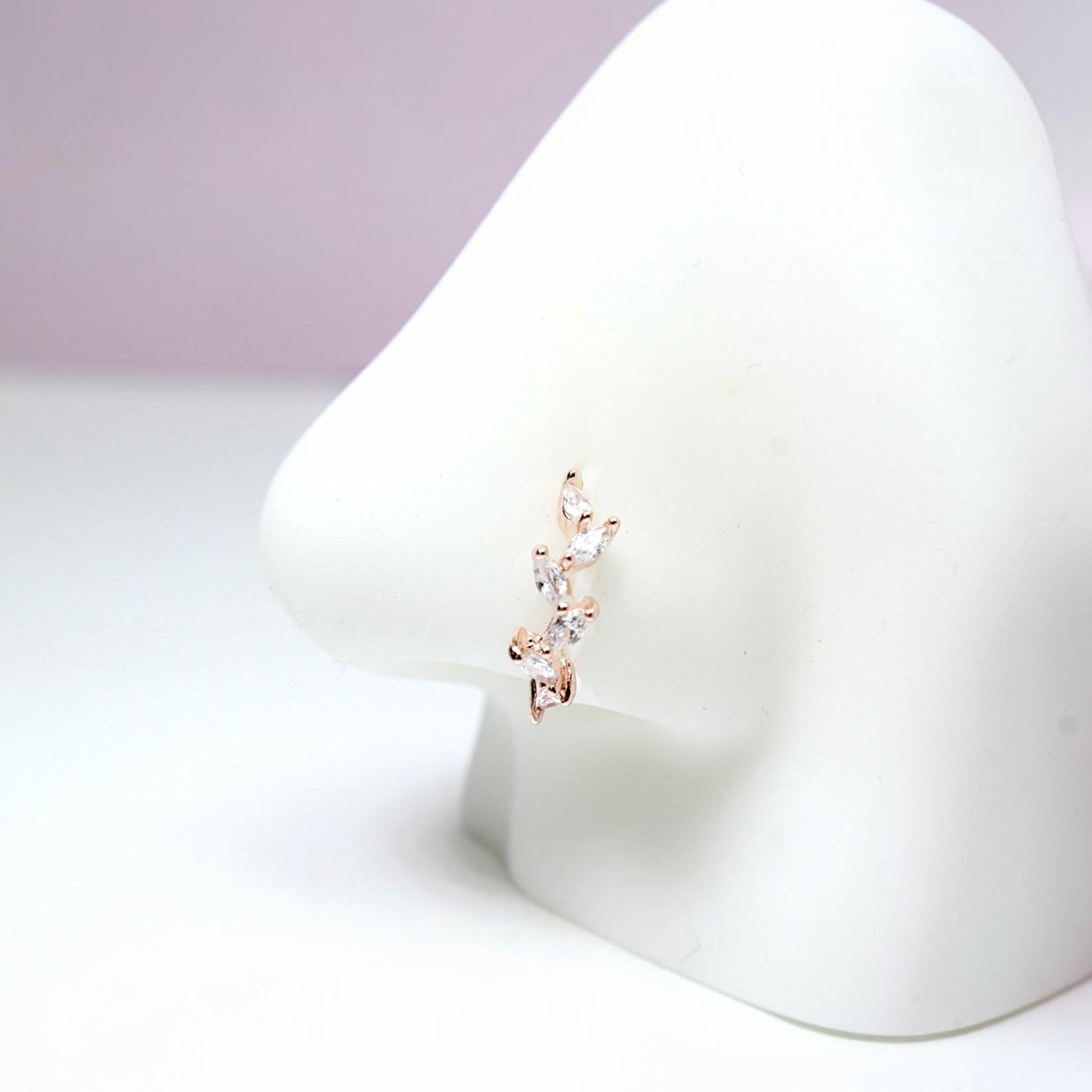 MKBodyJewelry 20g rose gold surgical steel nose hoop with a dainty CZ crystal leaf design on a white display model