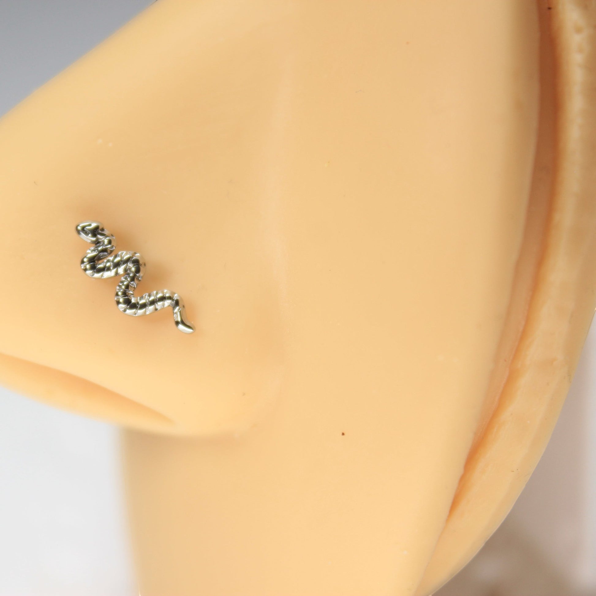 MKBodyJewelry silver snake nose stud on a mannequin nose, featuring a minimalist surgical steel L-bend design.