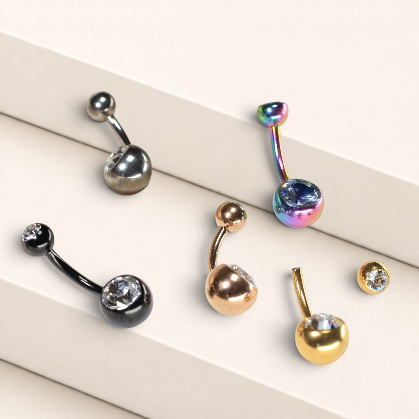 MKBodyJewelry titanium belly button rings with CZ jewels in various metallic finishes on a tiered display.