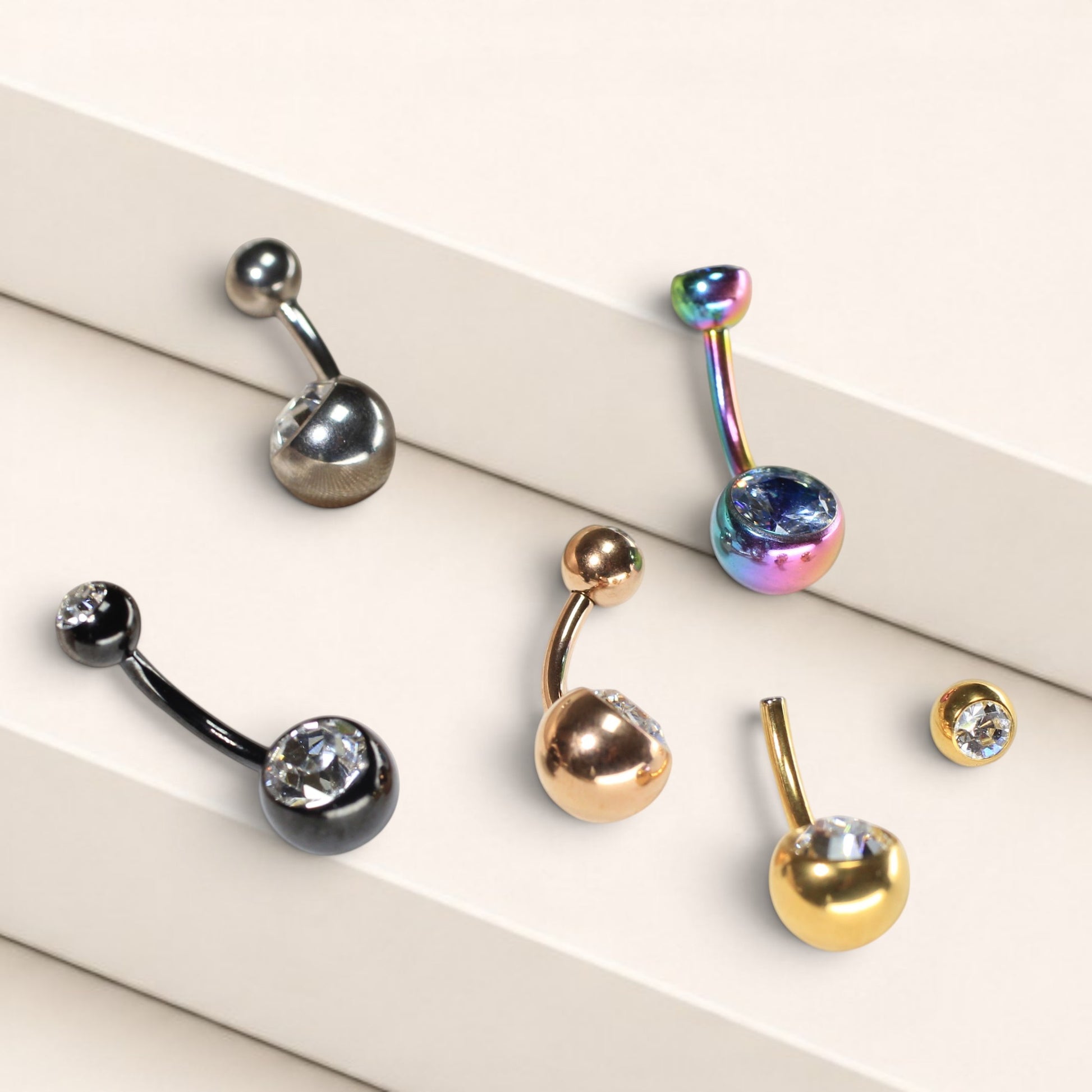 MKBodyJewelry titanium belly button rings with CZ jewels in various metallic finishes on a tiered display.