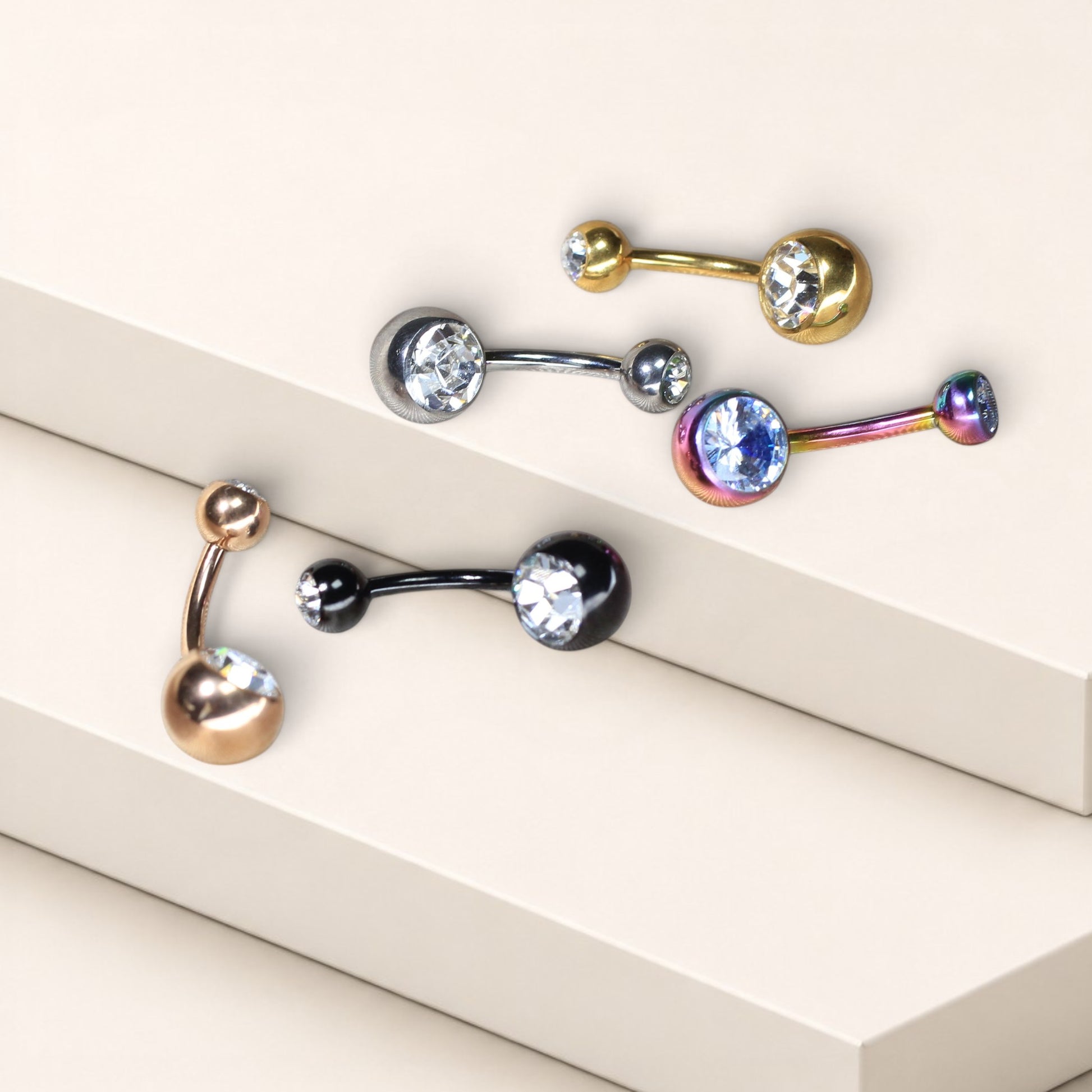 MKBodyJewelry titanium belly button rings with double CZ jewels in various metallic finishes on a tiered display.
