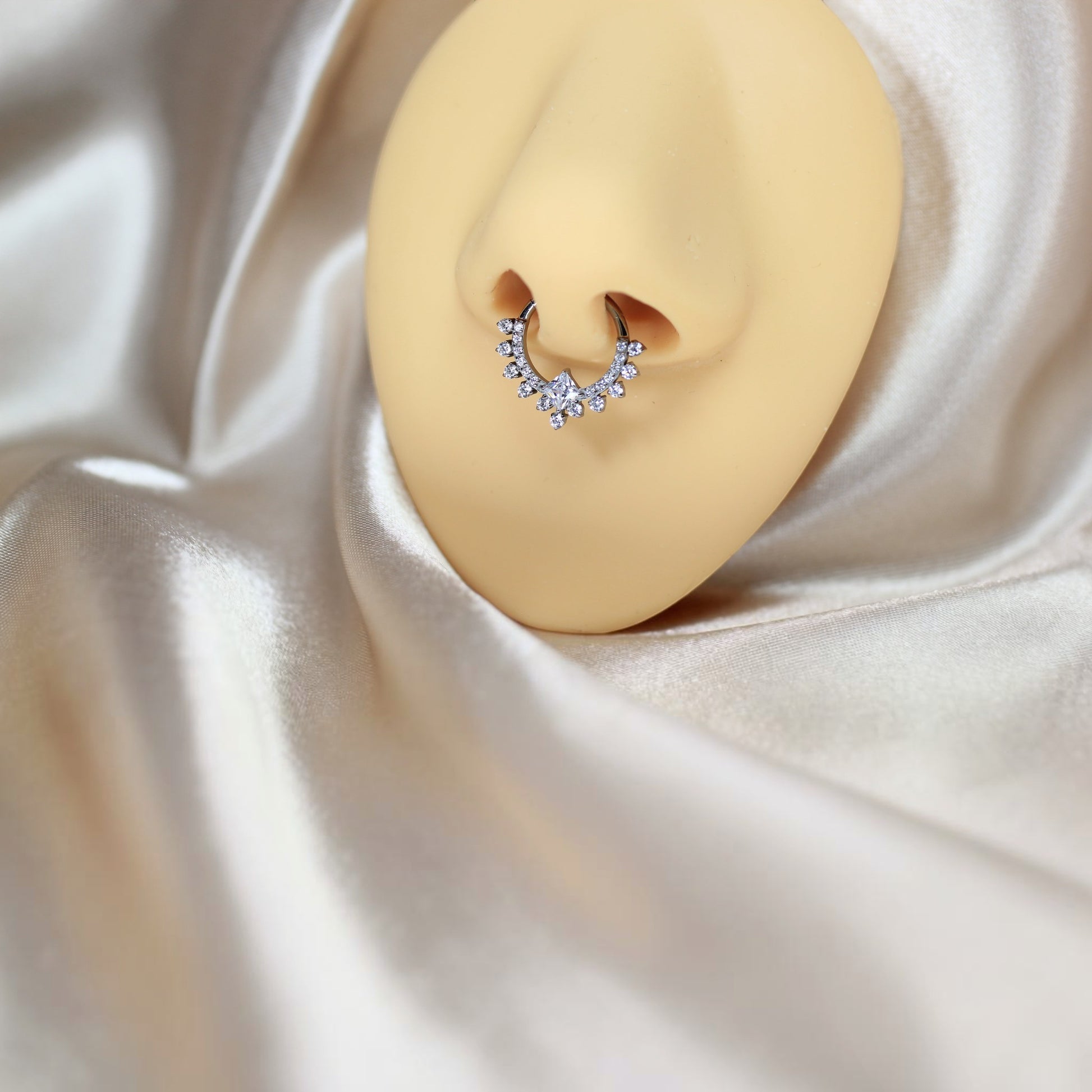 MKBodyJewelry titanium septum clicker ring with sparkling CZ stones on a nose mannequin against cream satin fabric.